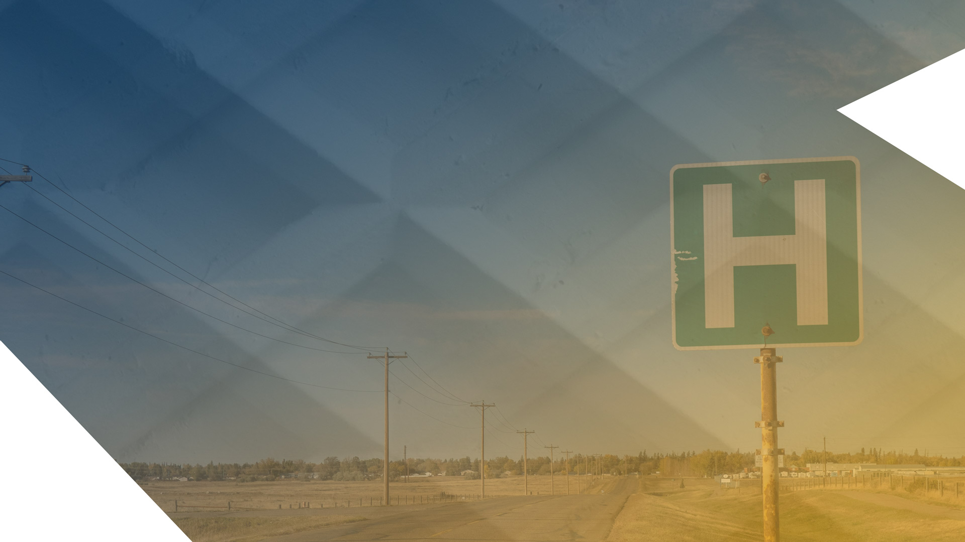 A young female nurse in blue scrubs smiles in a hospital corridor. The blurred out background has a group of nurses and doctors.